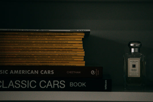 Perfume bottle resting on a shelf beside stacked books in soft indoor light